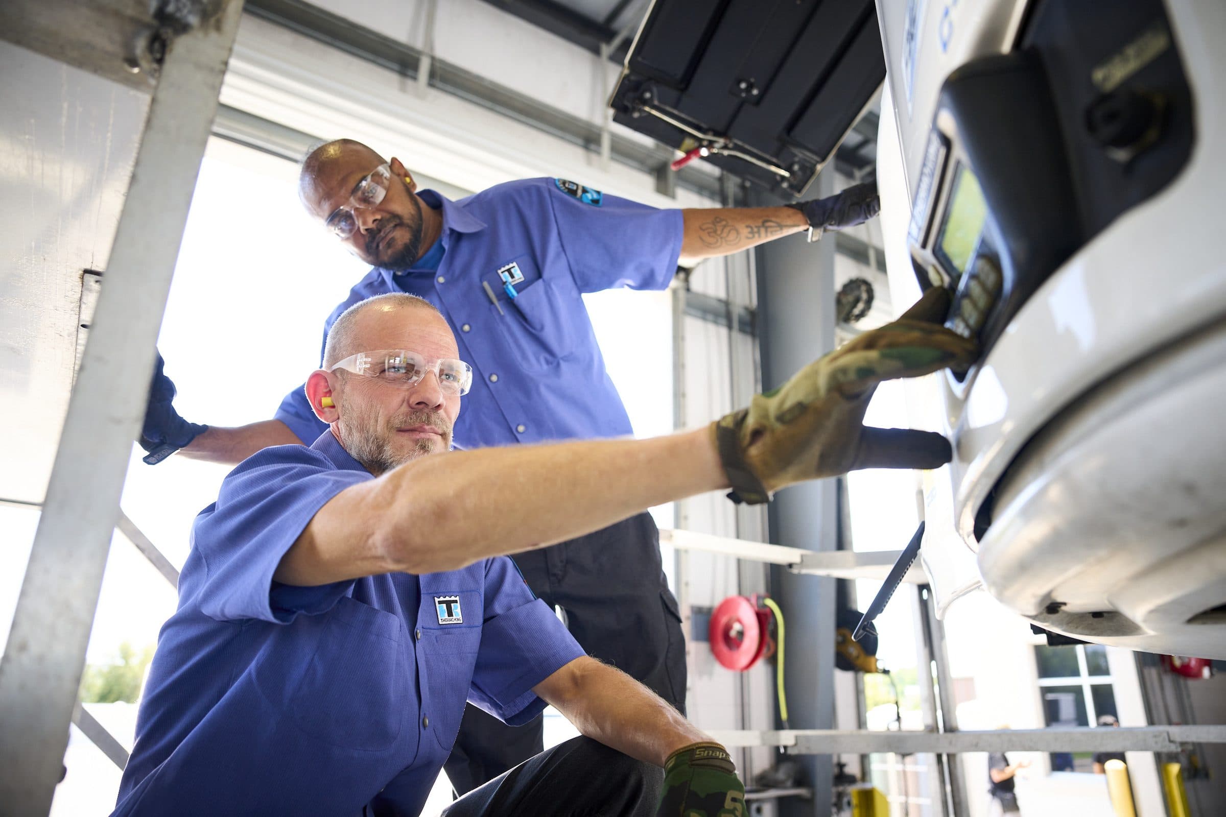 Two technicians in Thermo King shirts checking a trailer unit from a work stand